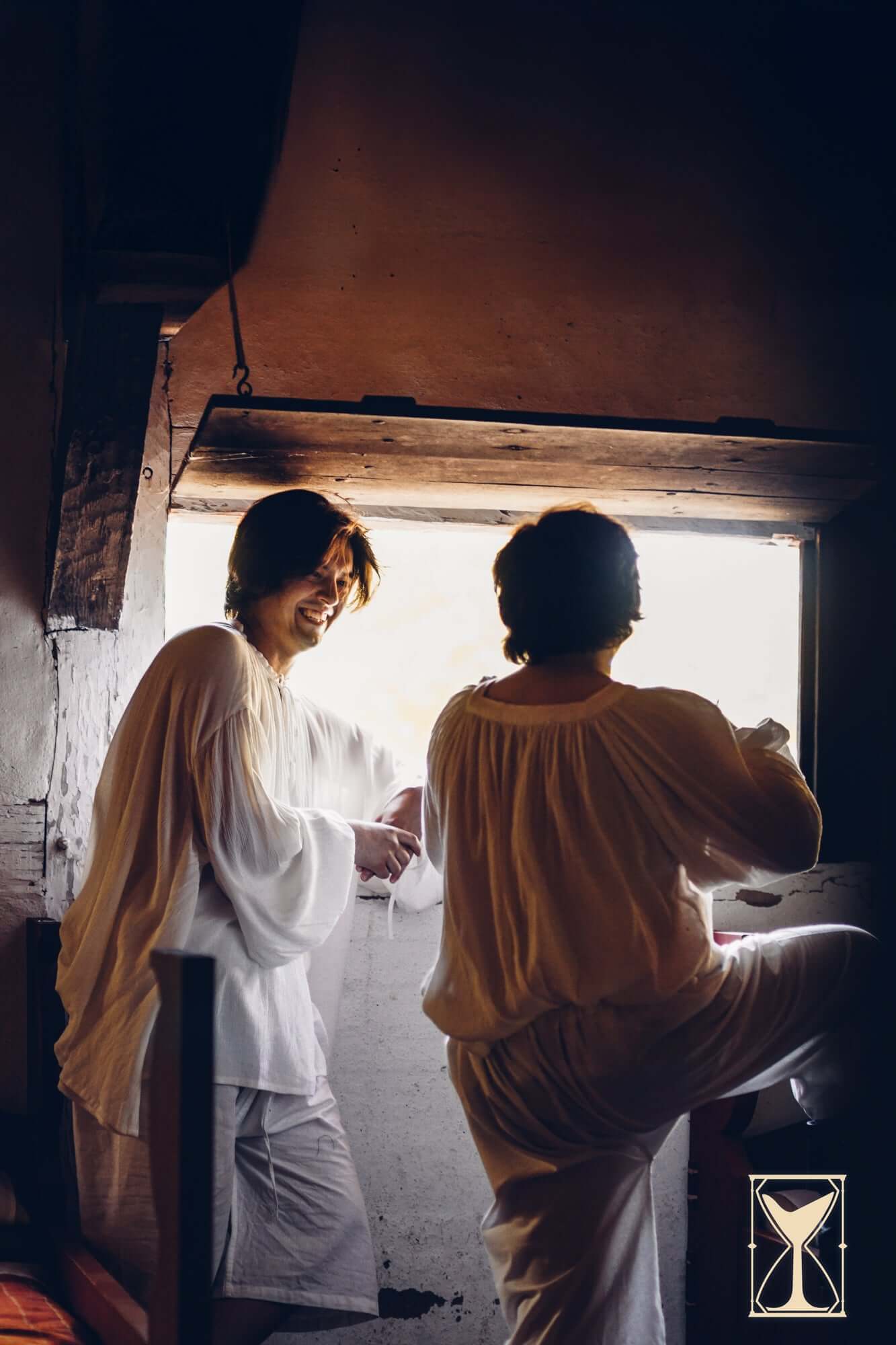 Two people wearing Braies - Long standing by a window in a medieval-inspired setting.