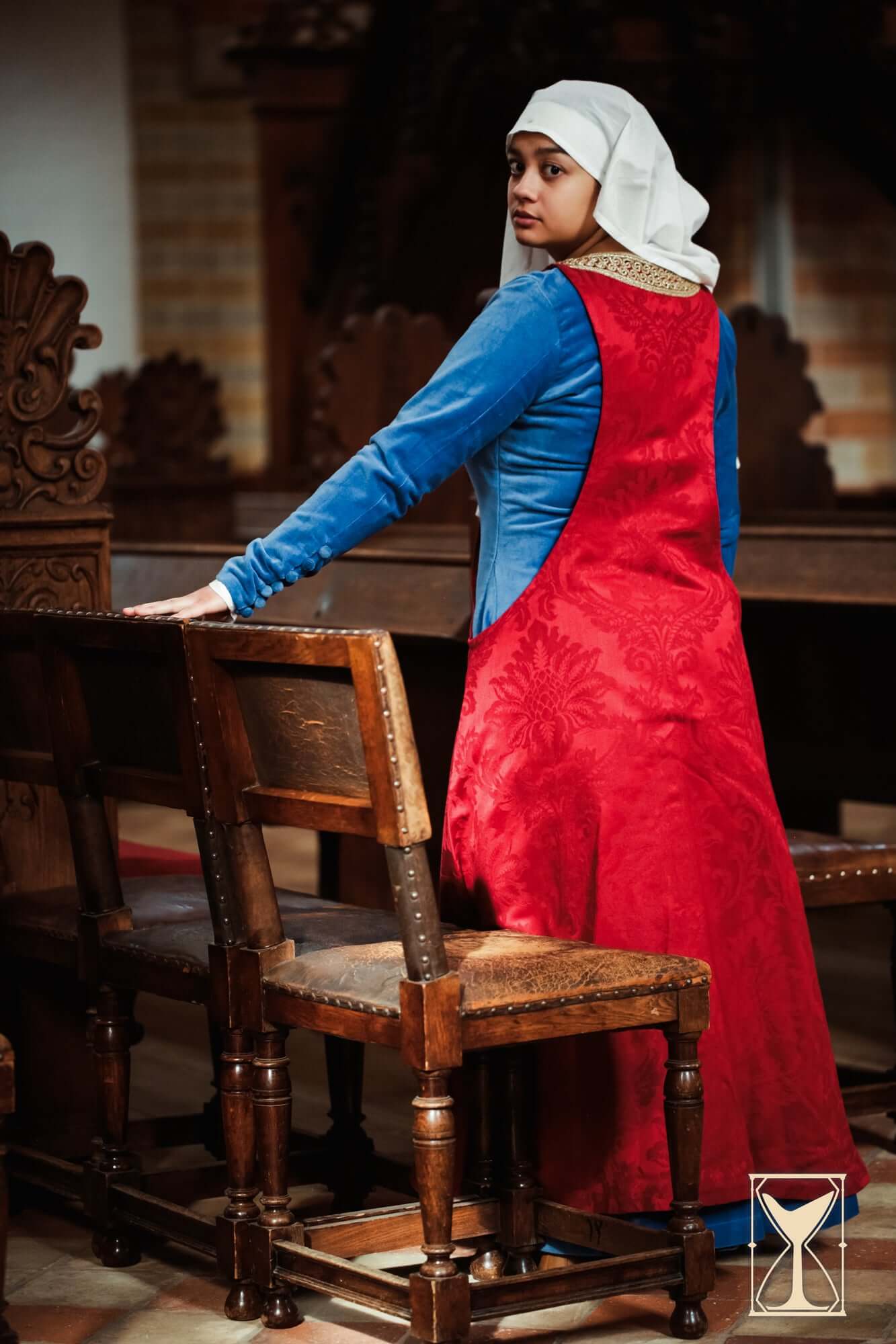 Pellote - Medieval Dress featuring a vibrant red surcoat over a blue tunic in a historical setting.