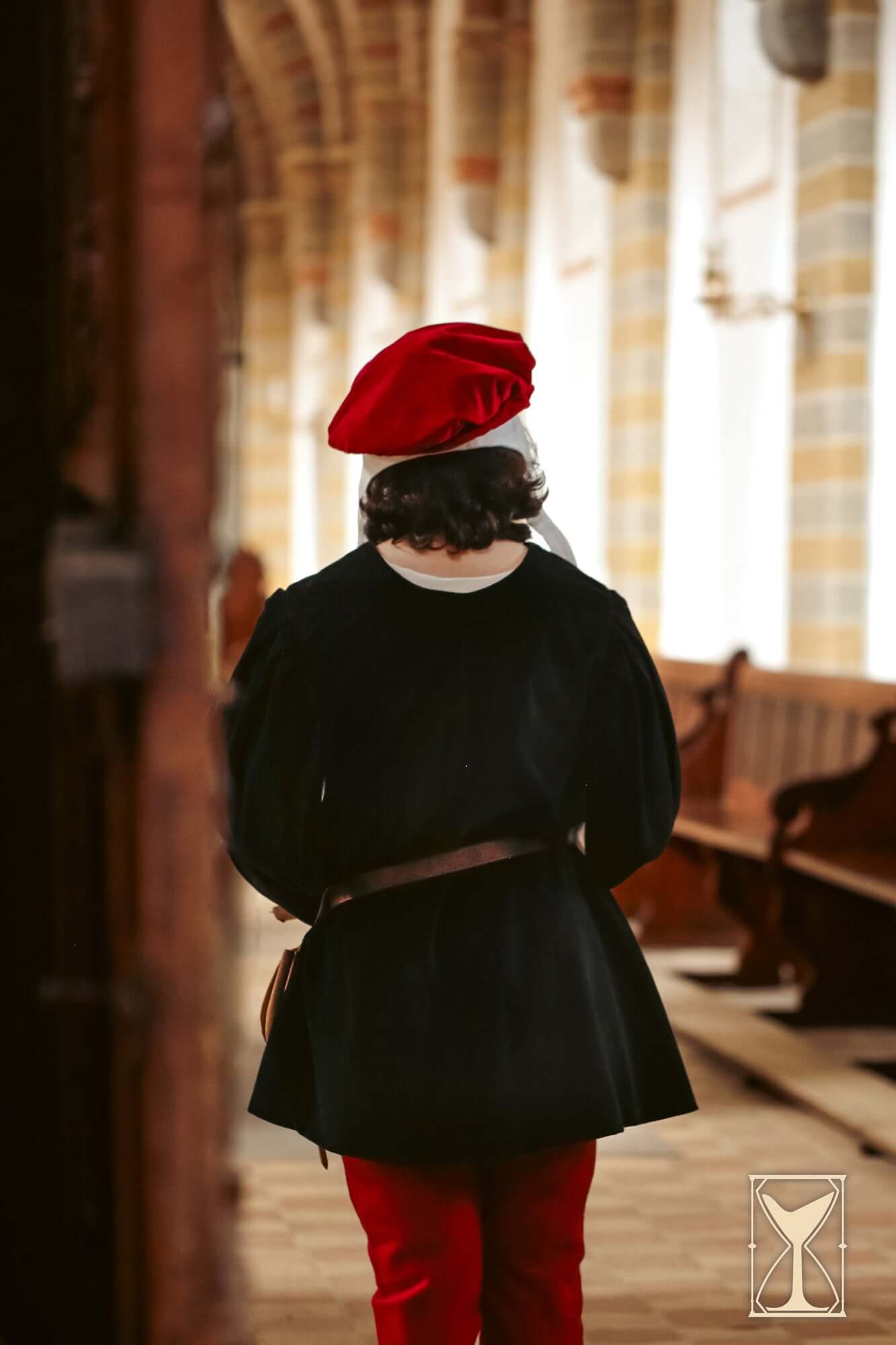 Person wearing a black Velvet Surcoat and red pants, viewed from the back in a medieval-style setting.