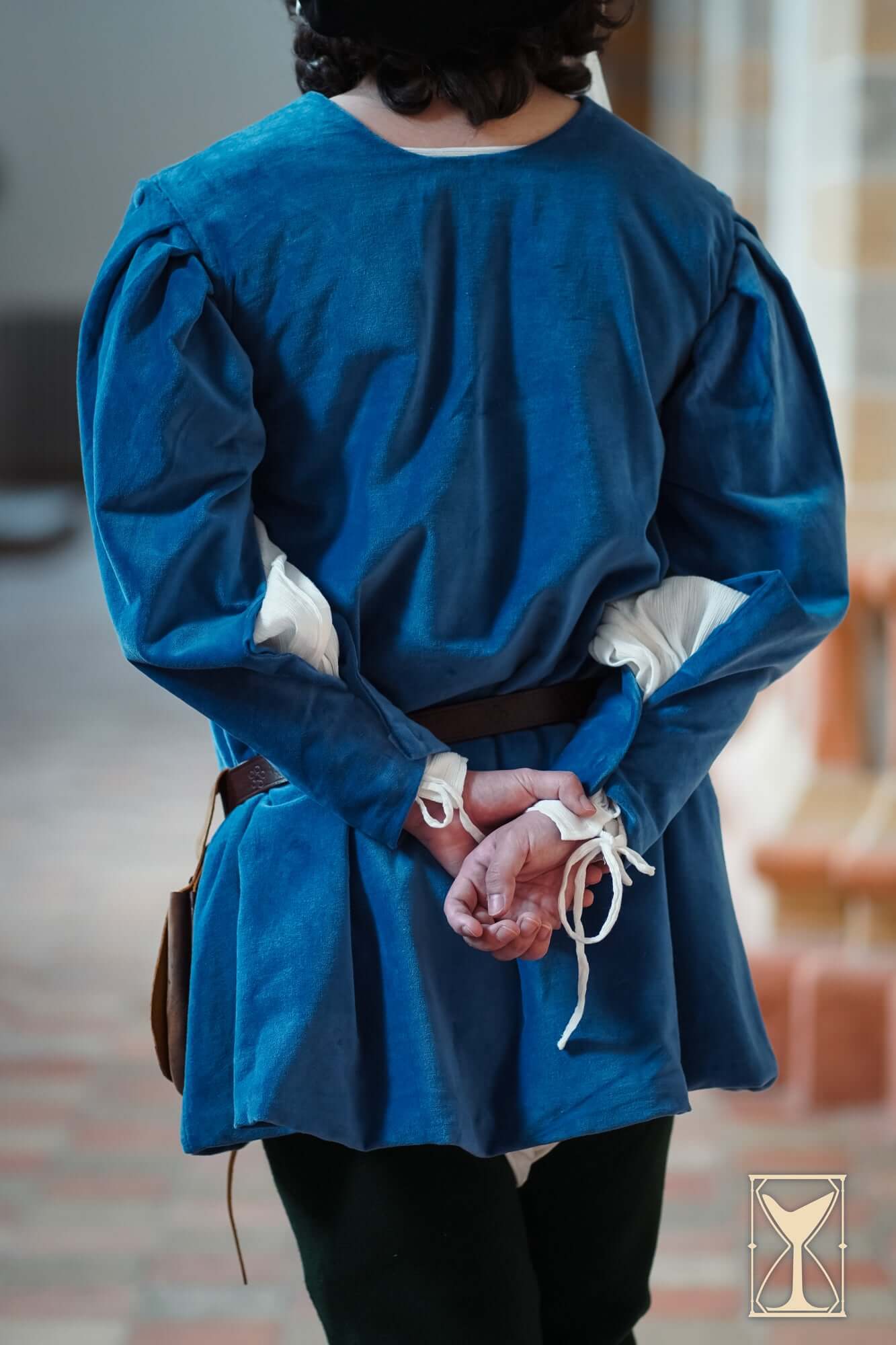 Person wearing a blue Velvet Surcoat with pulled sleeves, showcasing medieval-inspired attire from the back.