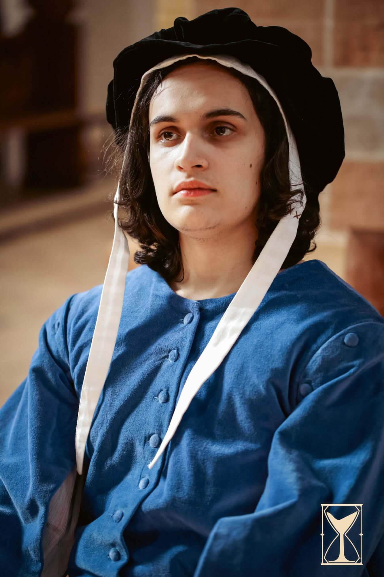 A young person in a blue velvet surcoat and black hat, embodying a medieval or fantasy character.