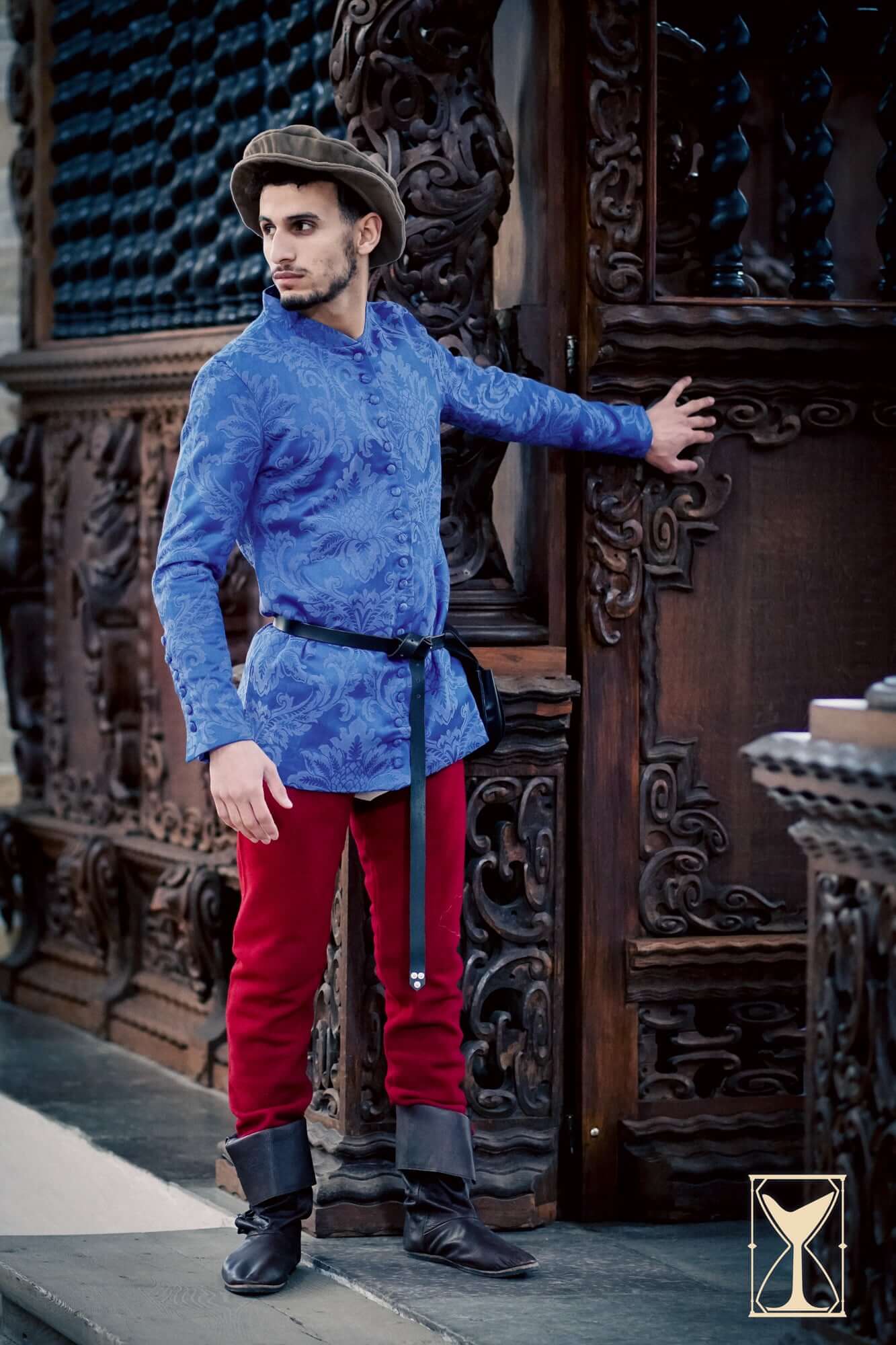 Cotehardie Rodrigo model wearing a blue brocade jacket with red pants, showcasing Late Middle Ages fashion.