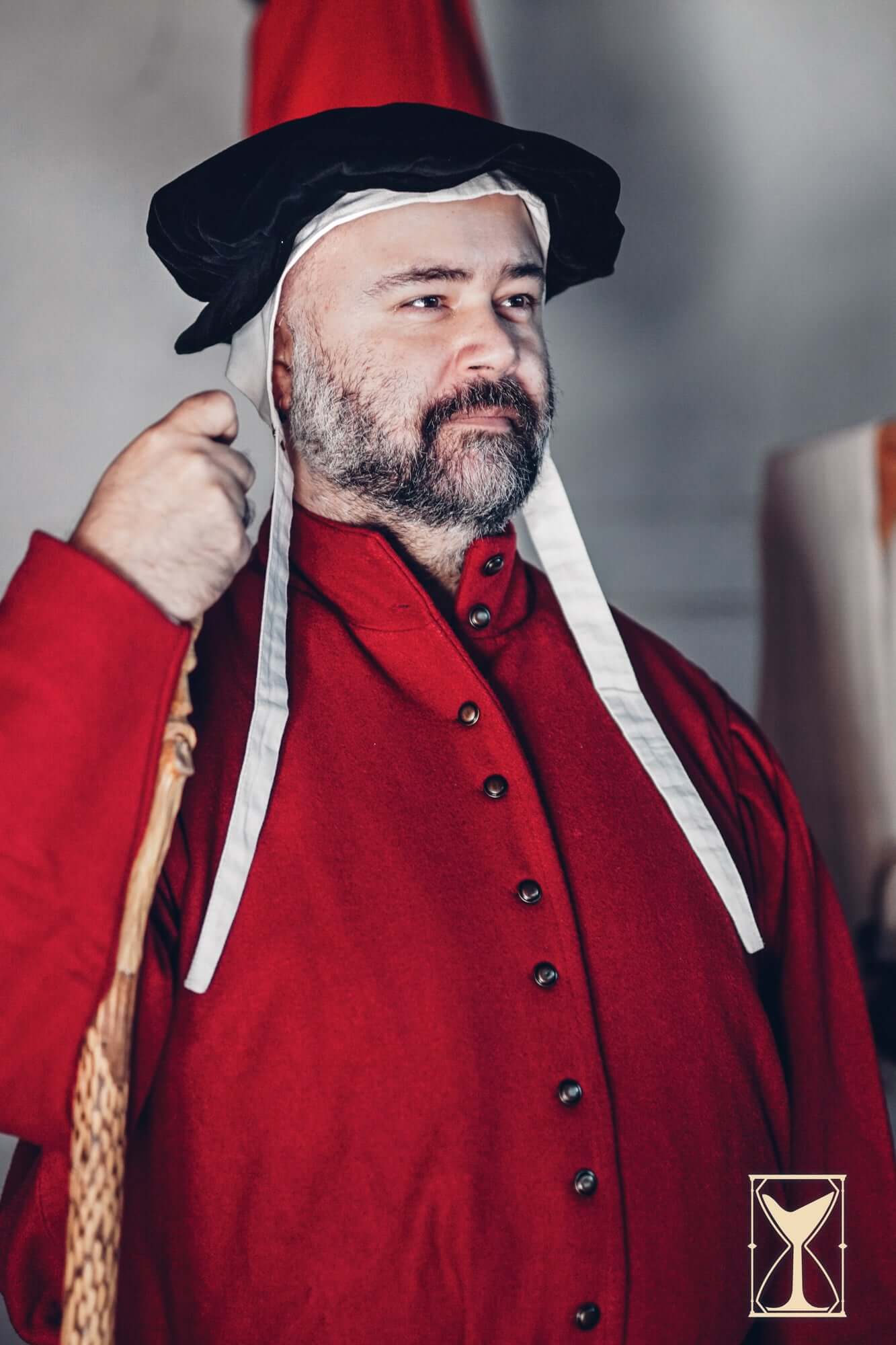Man wearing Beret Francisco, a historic velvet hat, dressed in 15th century attire with a red coat.