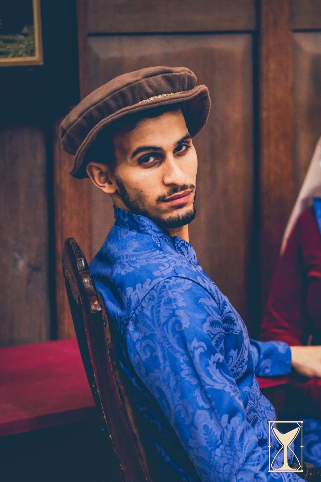 Model wearing the Flat Hat Edward and a blue patterned shirt in a Renaissance-inspired setting.
