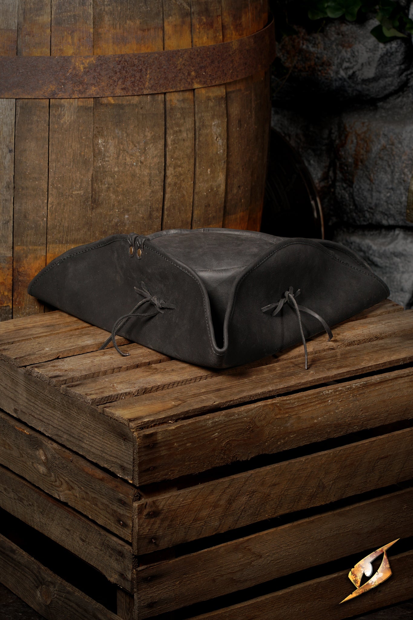 Simple Leather Pirate Tricorn Hat displayed on wooden crate with barrels in background.