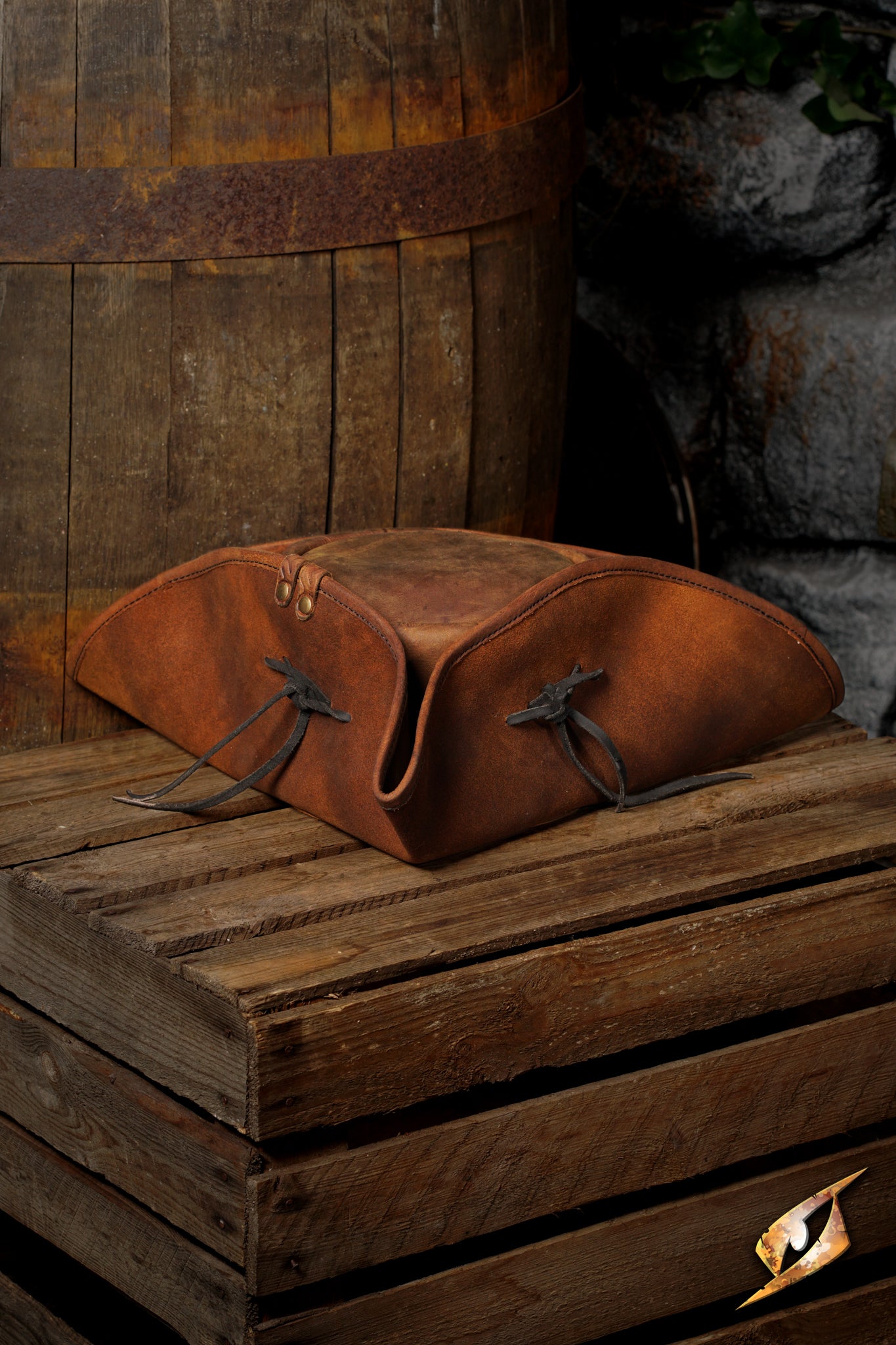 Simple Leather Pirate Tricorn Hat resting on a wooden crate near a barrel, showcasing its vintage design and craftsmanship.