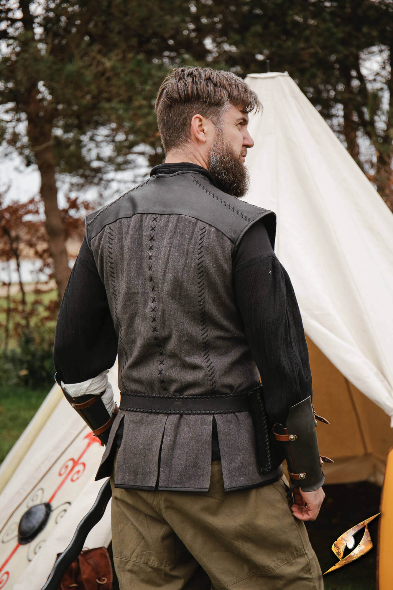 Man wearing a Rugged Canvas Jerkin with chrome leather shoulder reinforcement, standing by a tent.