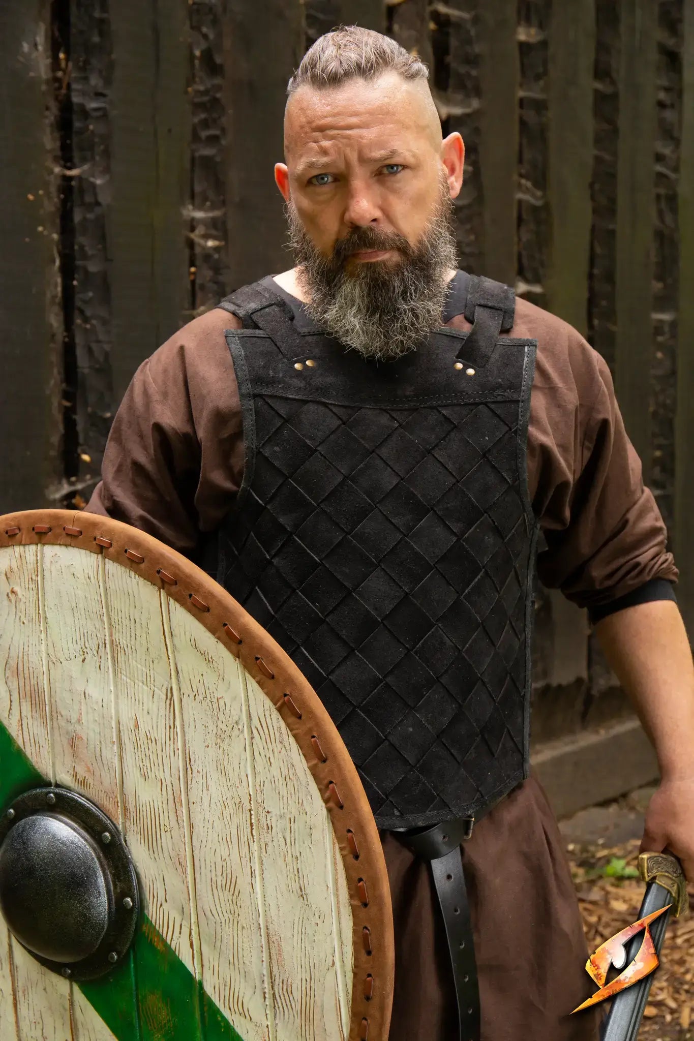 A warrior in a brown tunic stands confidently with the Thegn Shield, showcasing its round design and sturdy build.