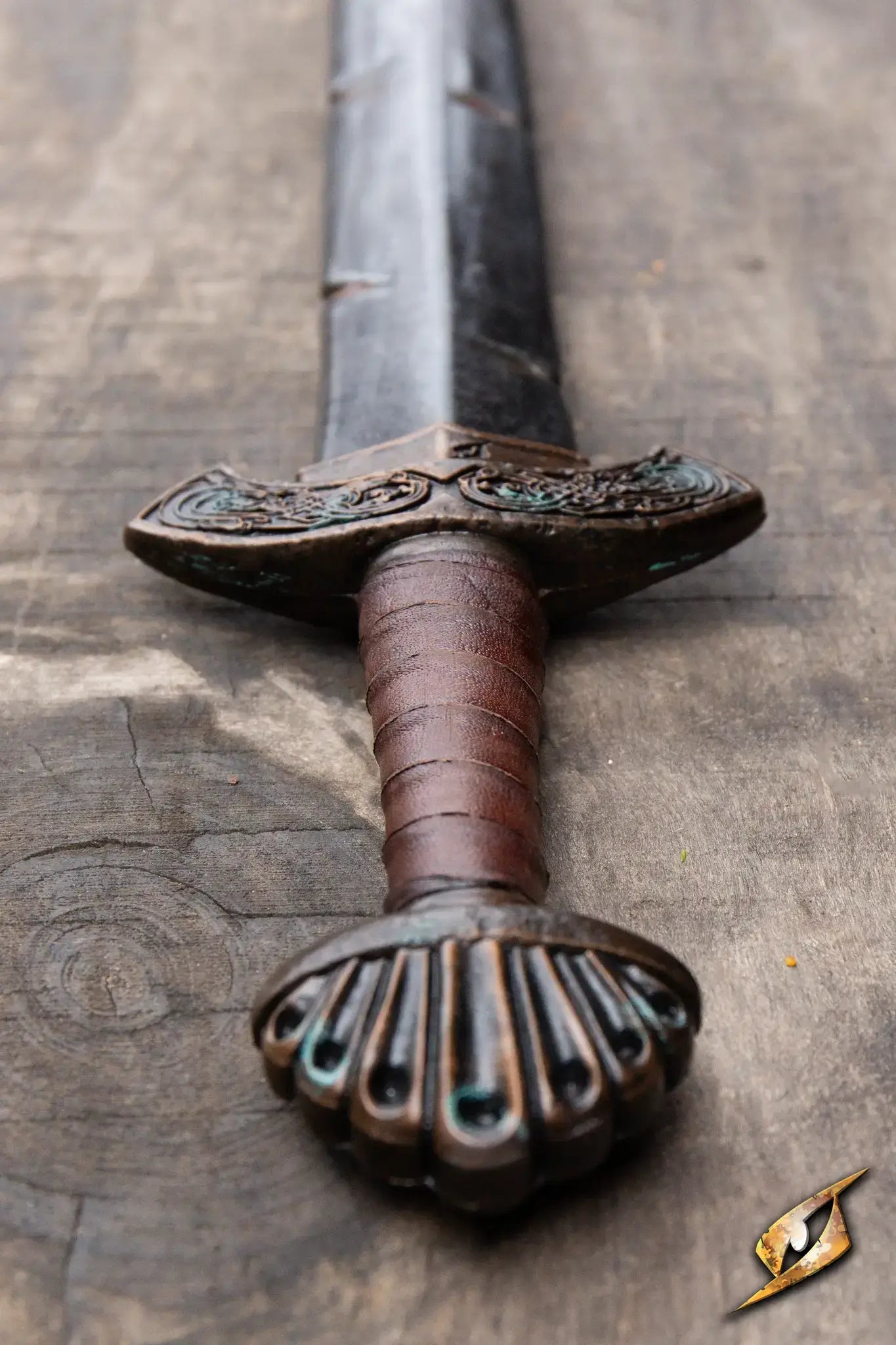 Battleworn Viking Sword resting on a wooden surface, showcasing its intricate hilt and fullered blade.