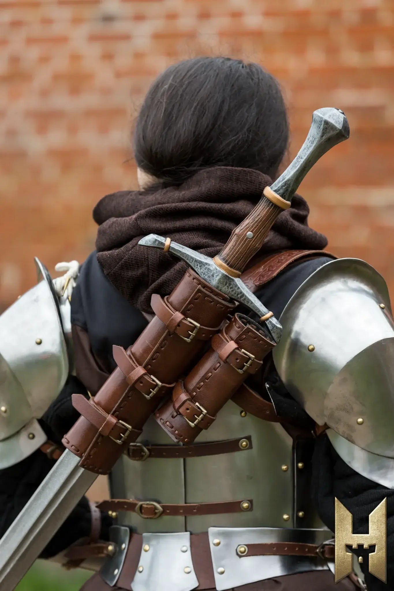 A person in armor with a brown cloak, showcasing the Bastard Sword sheathed on their back.