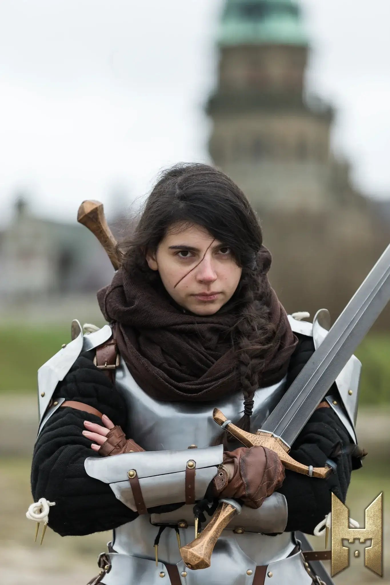 A warrior holding a Bastard Sword, dressed in armor with a leather scarf, set against a blurred city background.