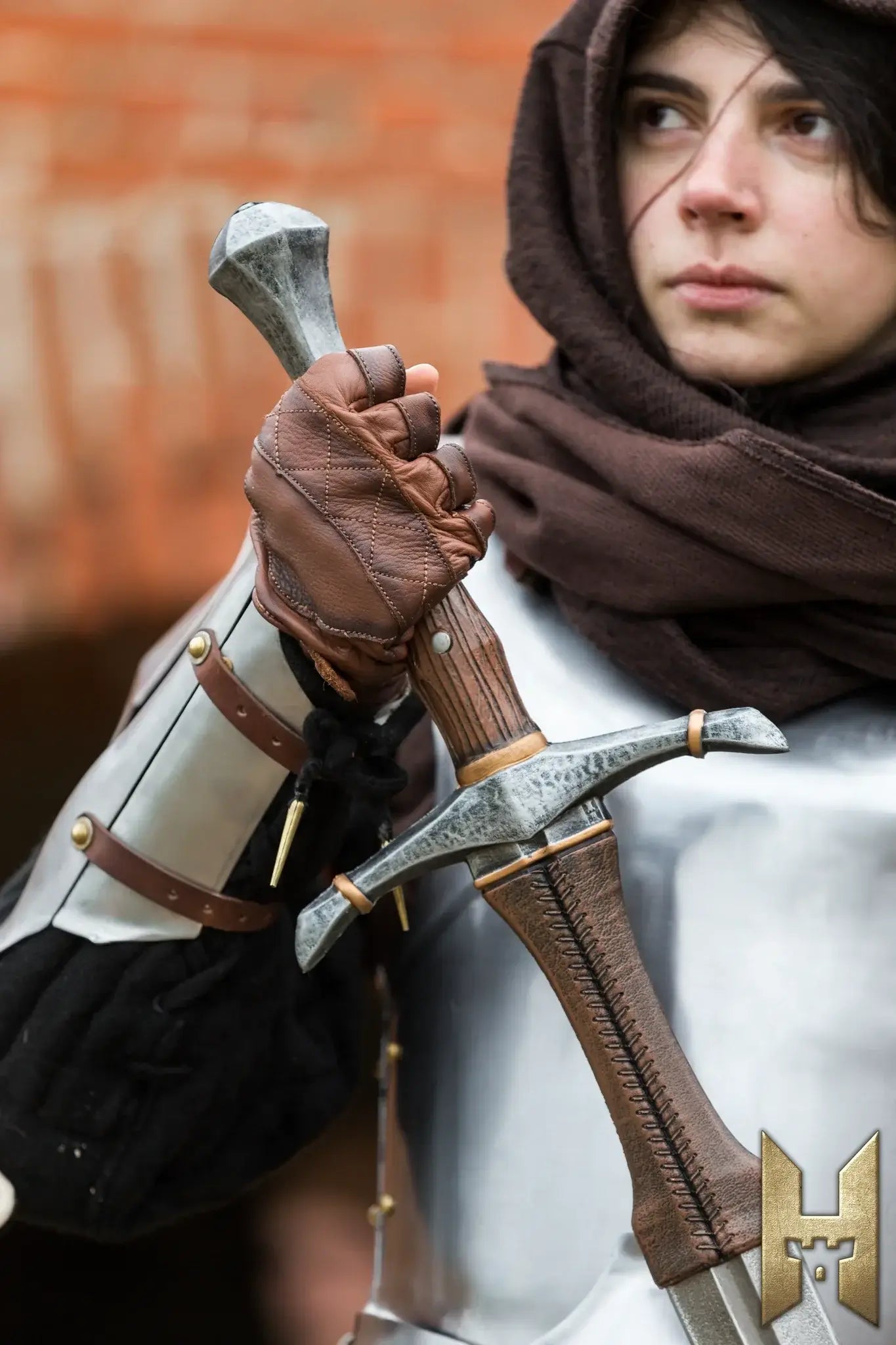 A person holding a Bastard Sword, dressed in medieval armor and a hood, showcasing the sword's intricate design.