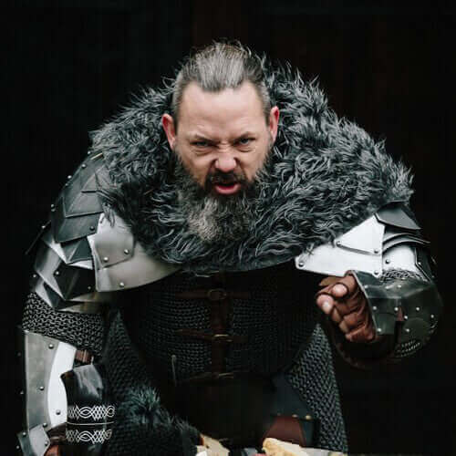 A fierce warrior in medieval armor, wearing a furry cloak, yelling and pointing, showcasing intensity and power.