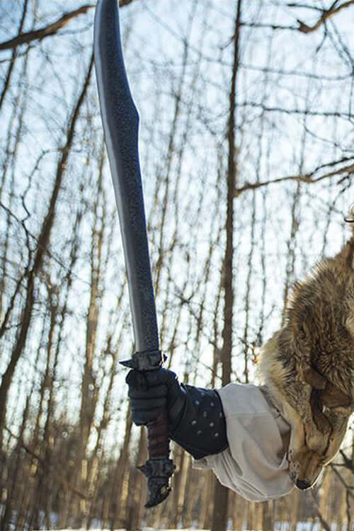 Person holding the Calimacil Baen Si II sword with hammered blade texture in a forest setting.