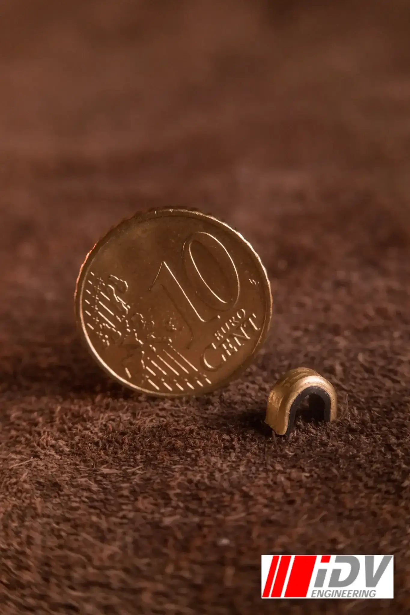 Close-up of a 10-cent coin next to a small brass String Nock Marker on a textured background.