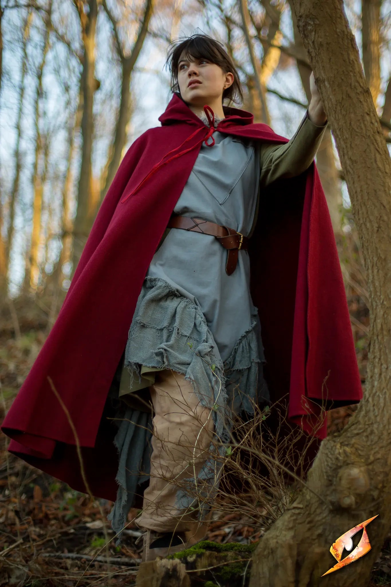 A model wearing a red Cape Wool cape in a forest, showcasing its stylish hood and comfortable fit.
