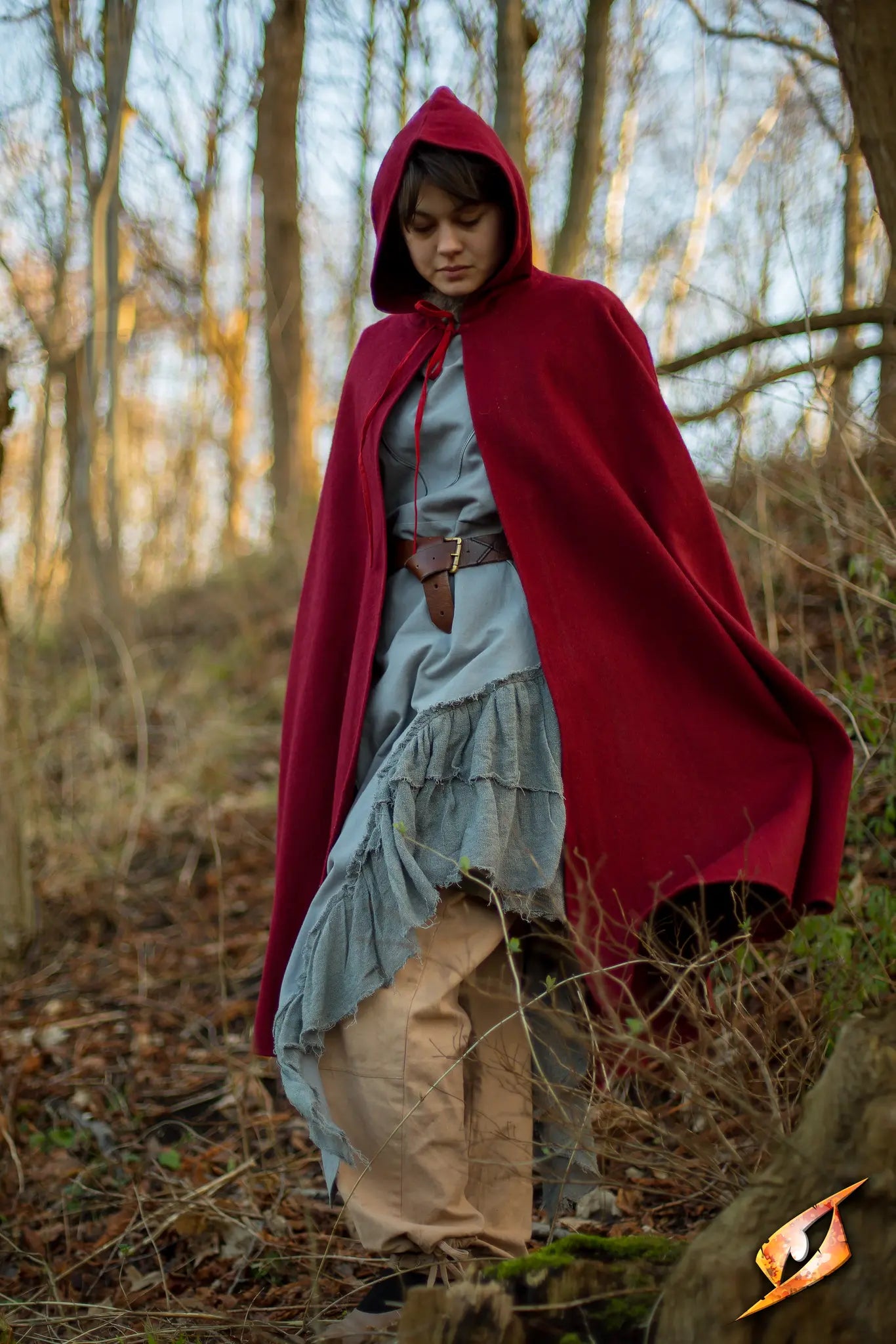 Model wearing a red Cape Wool in a forest setting, showcasing the elegant design and deep hood.