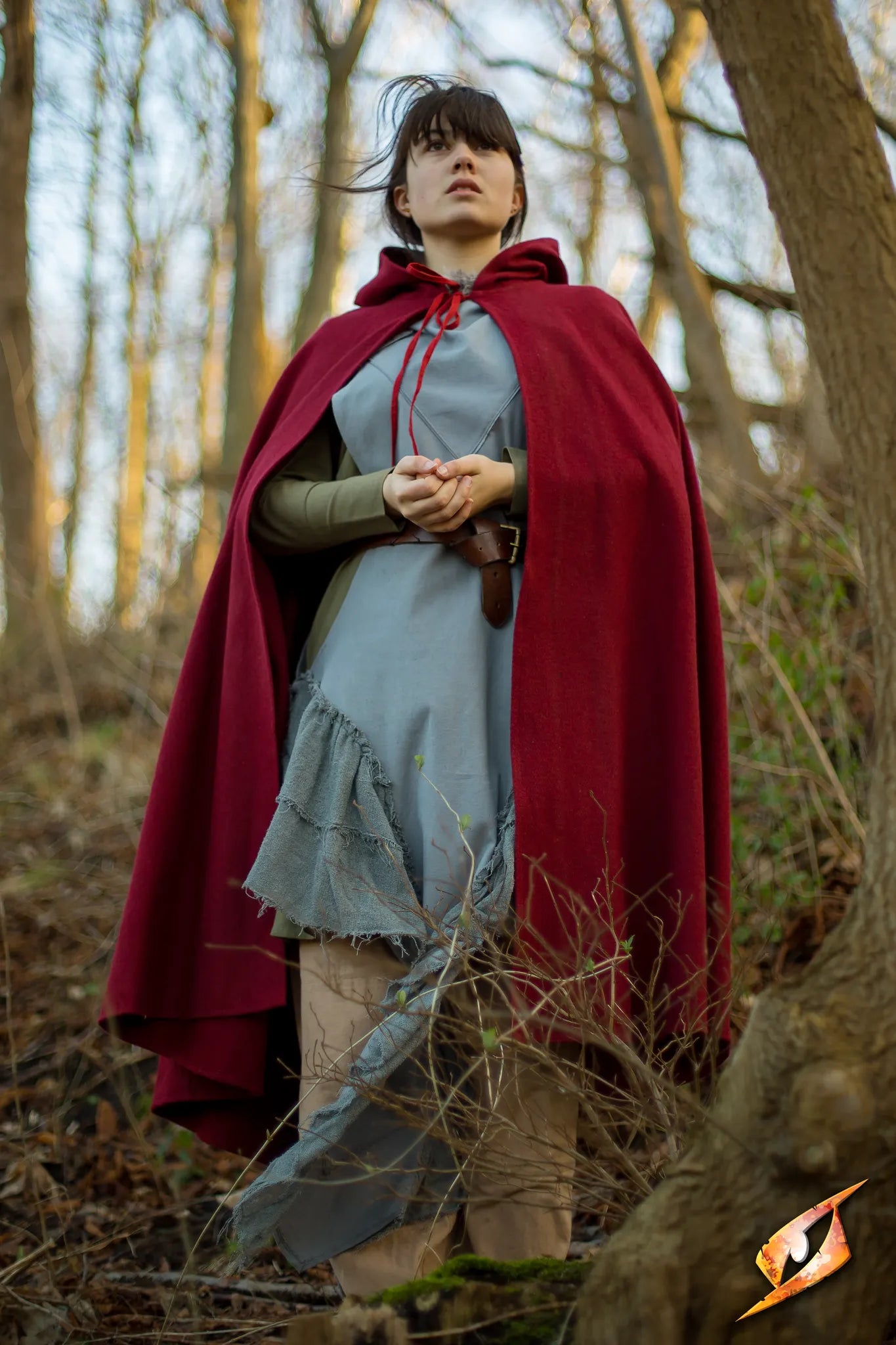 Model wearing Cape Wool in a forest setting, showcasing the deep hood and flowing design of the cape.