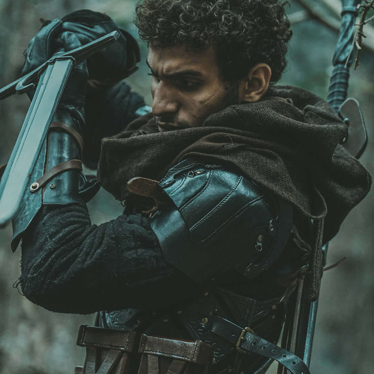 Warrior preparing for battle, dressed in leather armor with a sword and cloak, amidst a forest setting.
