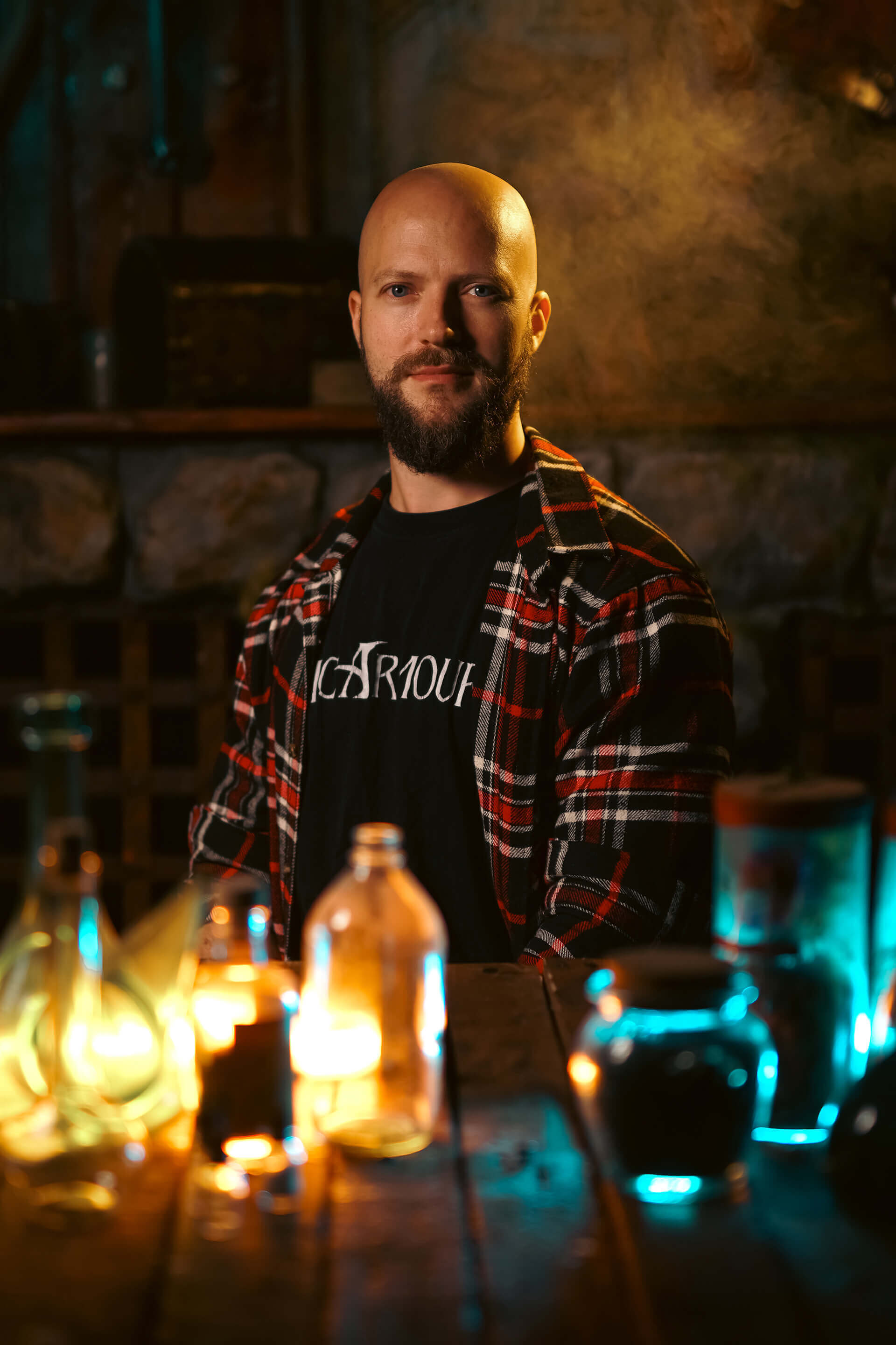 A bearded man in a plaid shirt sits at a table filled with colorful glowing bottles, creating a moody atmosphere.
