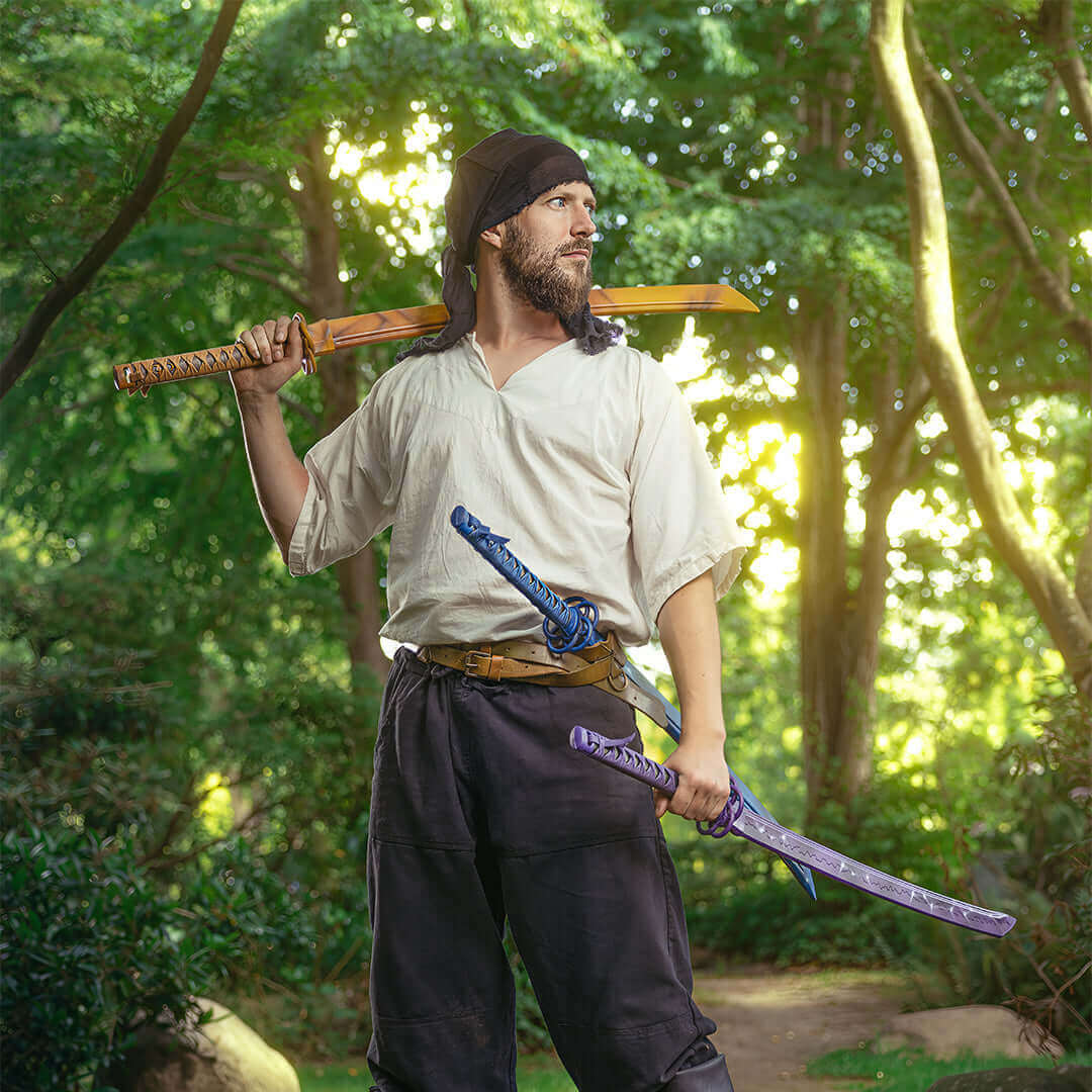 A man dressed as a pirate stands in a forest, holding two swords, showcasing a brave pose.