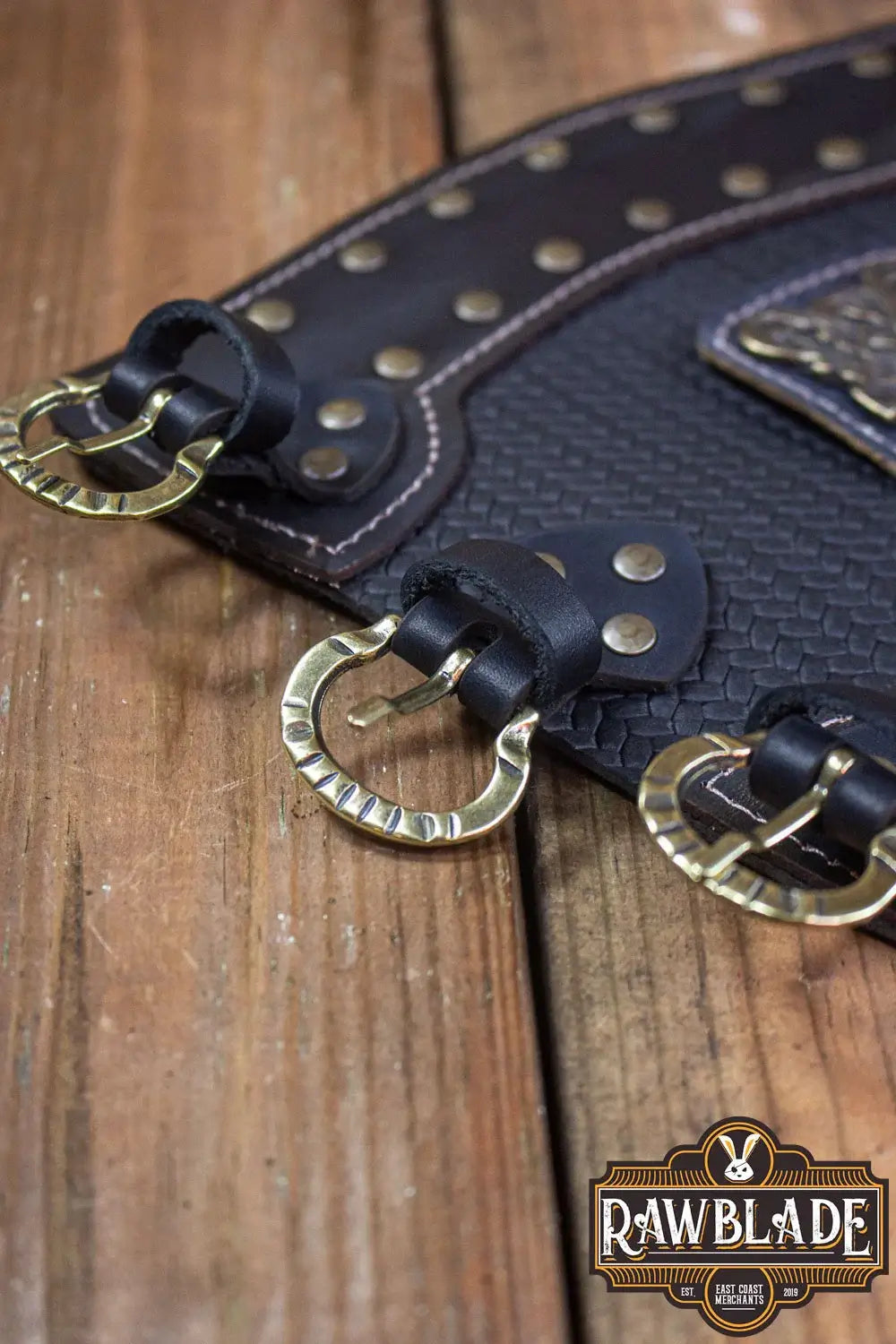 Close-up of Bruce Bracers featuring leather, rivets, and buckles on a wooden surface.