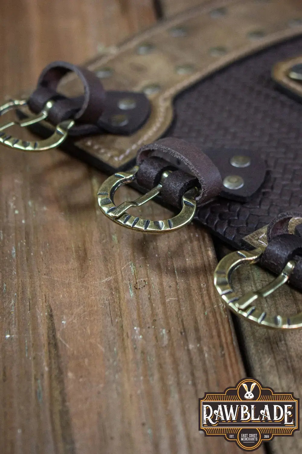 Close-up of Bruce Bracers with leather straps and metal rings on a wooden surface.