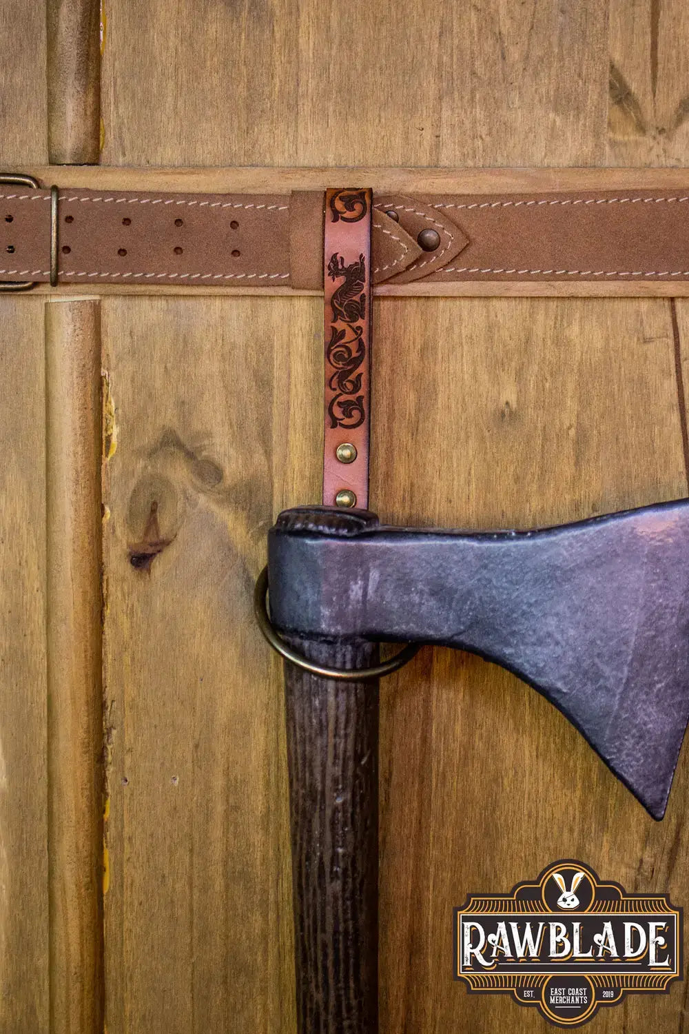 Aquitania Ring Holder displaying ornate leather engraving supporting an axe against a wooden background.