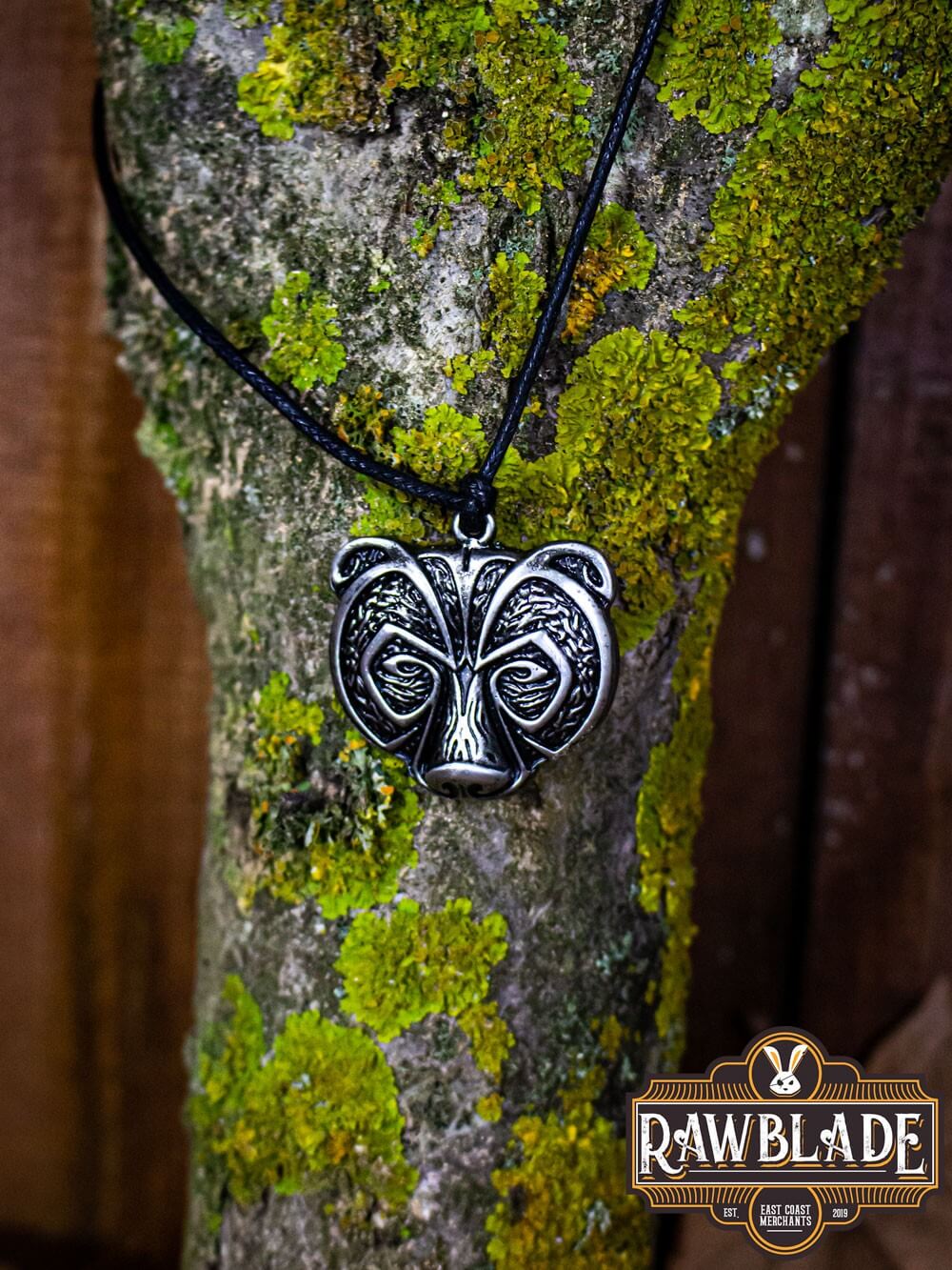 Bear Clan Pendant showcasing a bear's head design, symbolizing strength, hanging on a black cord against a mossy tree.