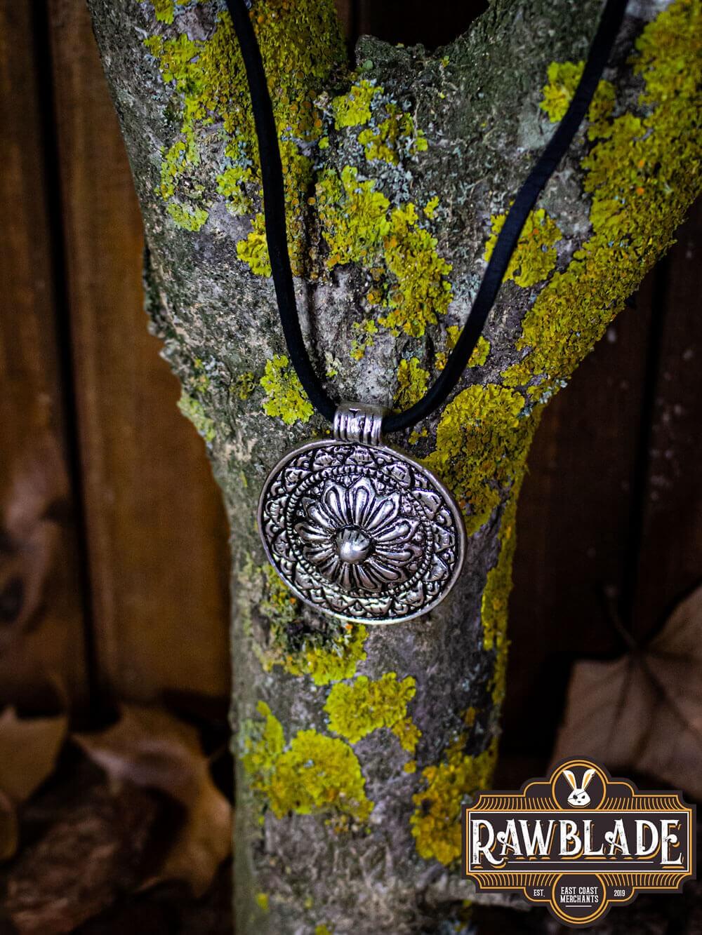 Capadocian Amulet on a black cord necklace, featuring intricate floral design and circular pendant, displayed on a mossy tree.