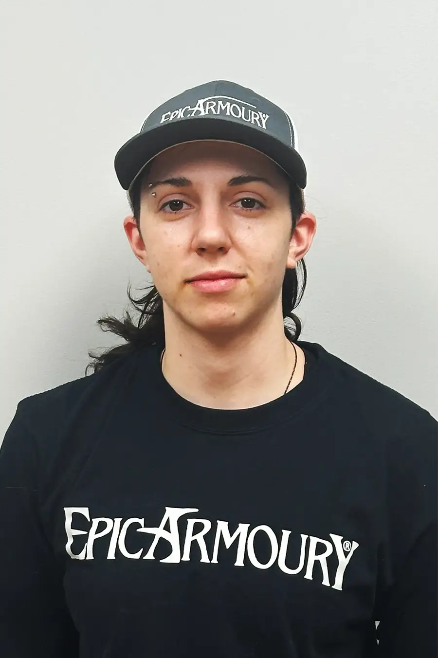 Person wearing Epic Armoury cap and shirt, showcasing brand apparel and style in a neutral background.