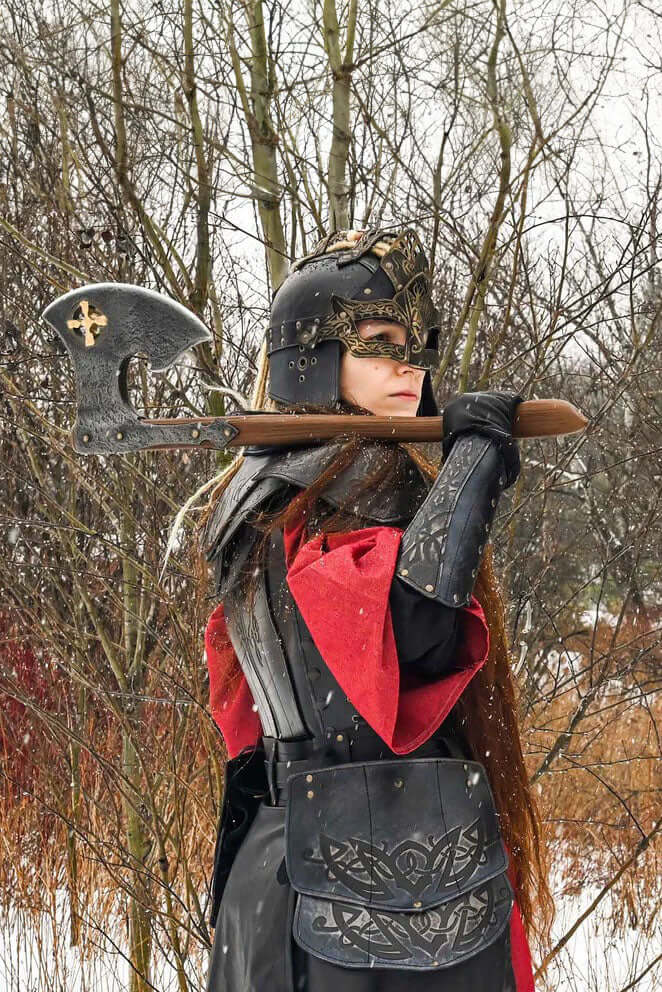A warrior in armor holding the Baruk II axe, featuring a steel head and golden cross, against a winter backdrop.