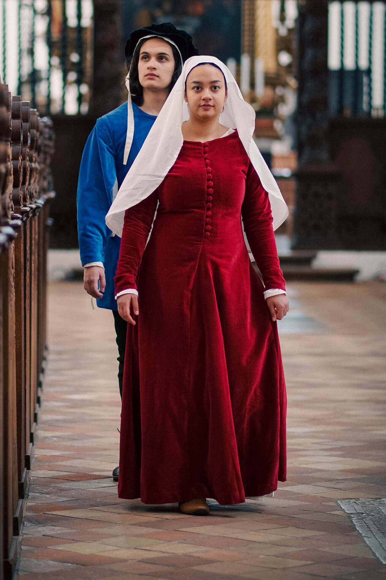 Two people in period costumes walking through a cathedral.