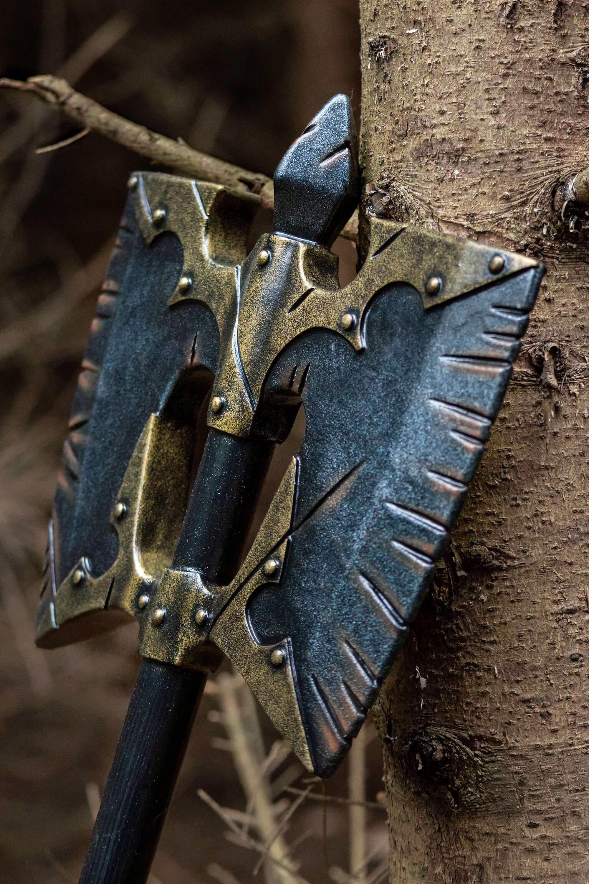 Decorative axe head with a metallic finish, leaning against a tree