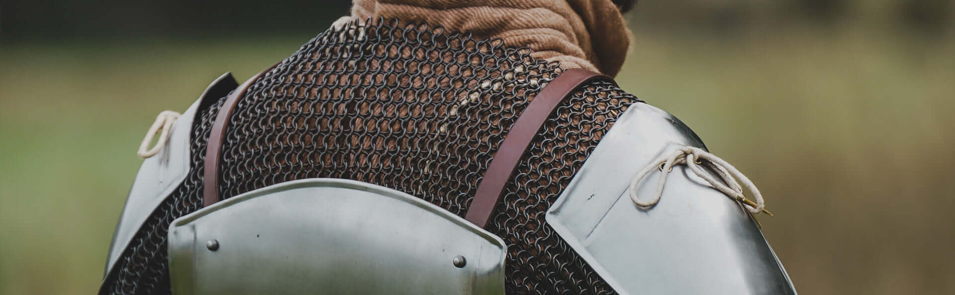 Close-up of a person wearing chainmail armor and shoulder plates outdoors, showcasing historical medieval attire.