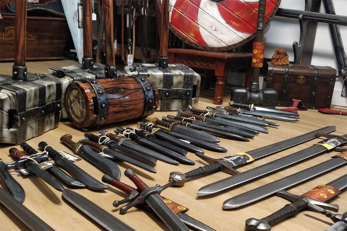 Collection of various swords and weapons displayed with decorative trunks and crates in a historical setting.