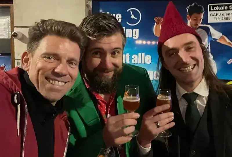 Three men smiling outdoors, holding drinks, celebrating together in colorful festive attire.