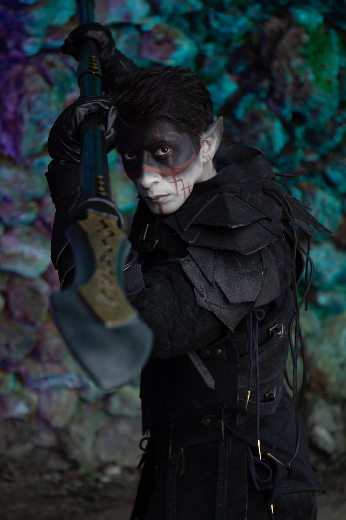Person in dark costume holding a weapon against a colorful, textured wall.
