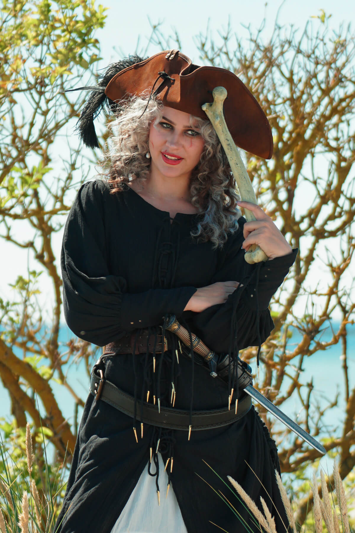 Person in pirate costume holding a bone with trees and sky in the background