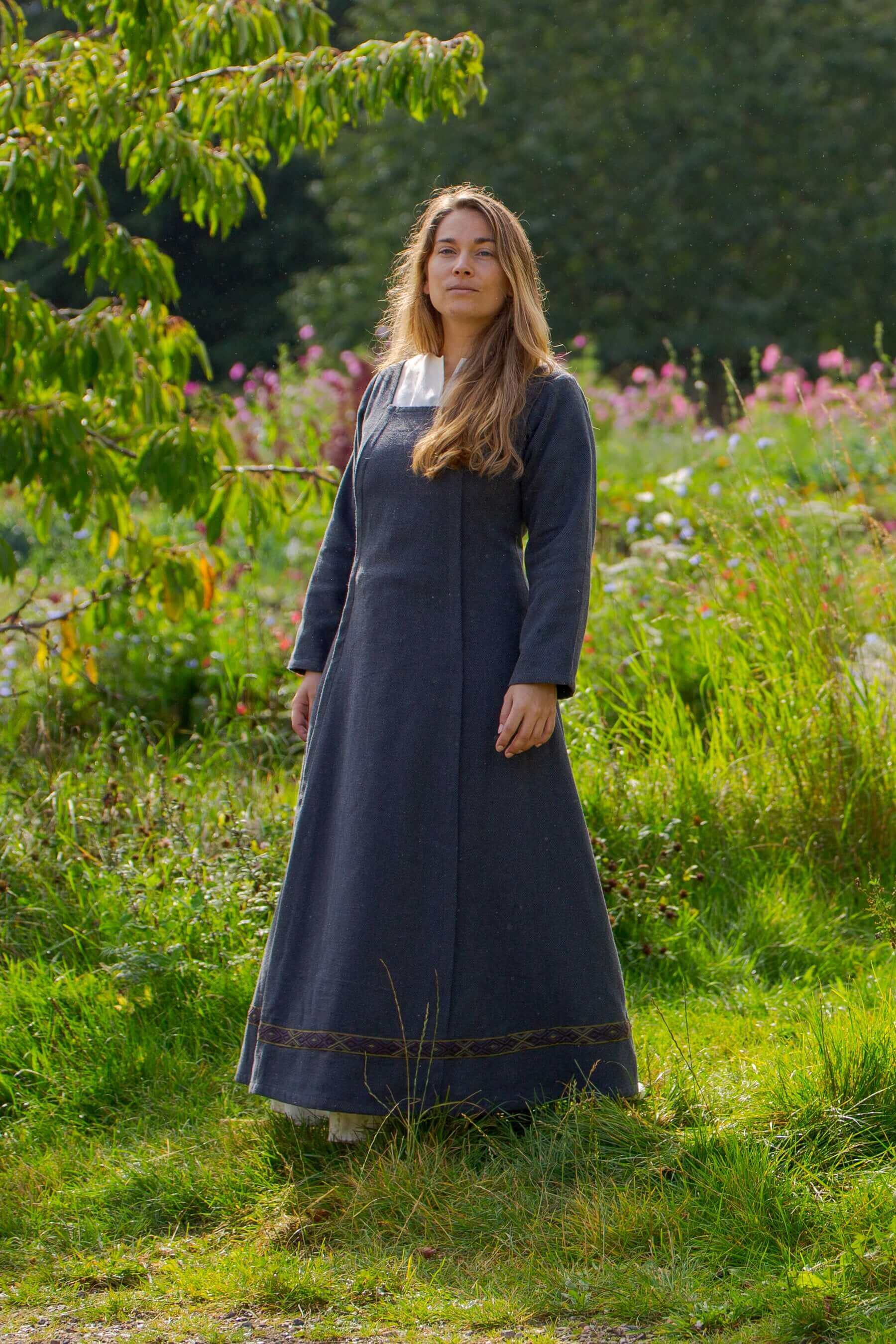 Woman in a long dark blue dress standing in a natural setting with greenery and flowers.