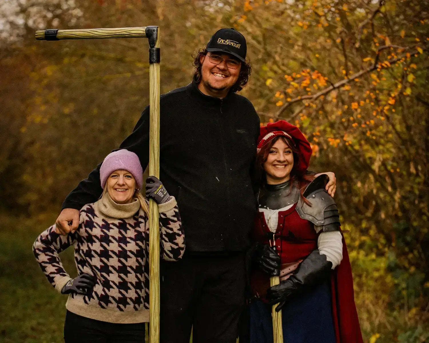 Three friends posing outdoors, one in armor, surrounded by autumn foliage during a photoshoot.