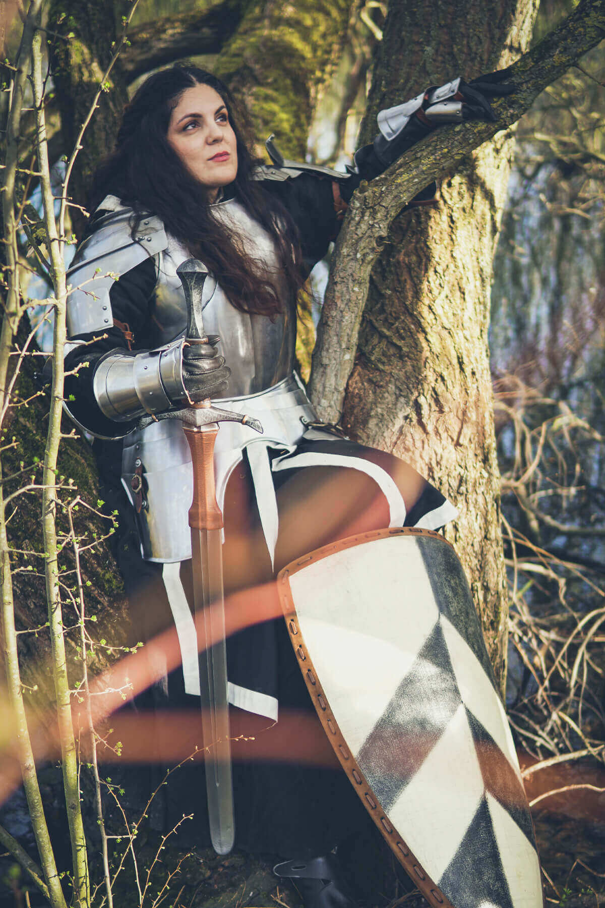 Person in medieval armor sitting against a tree in a forest setting