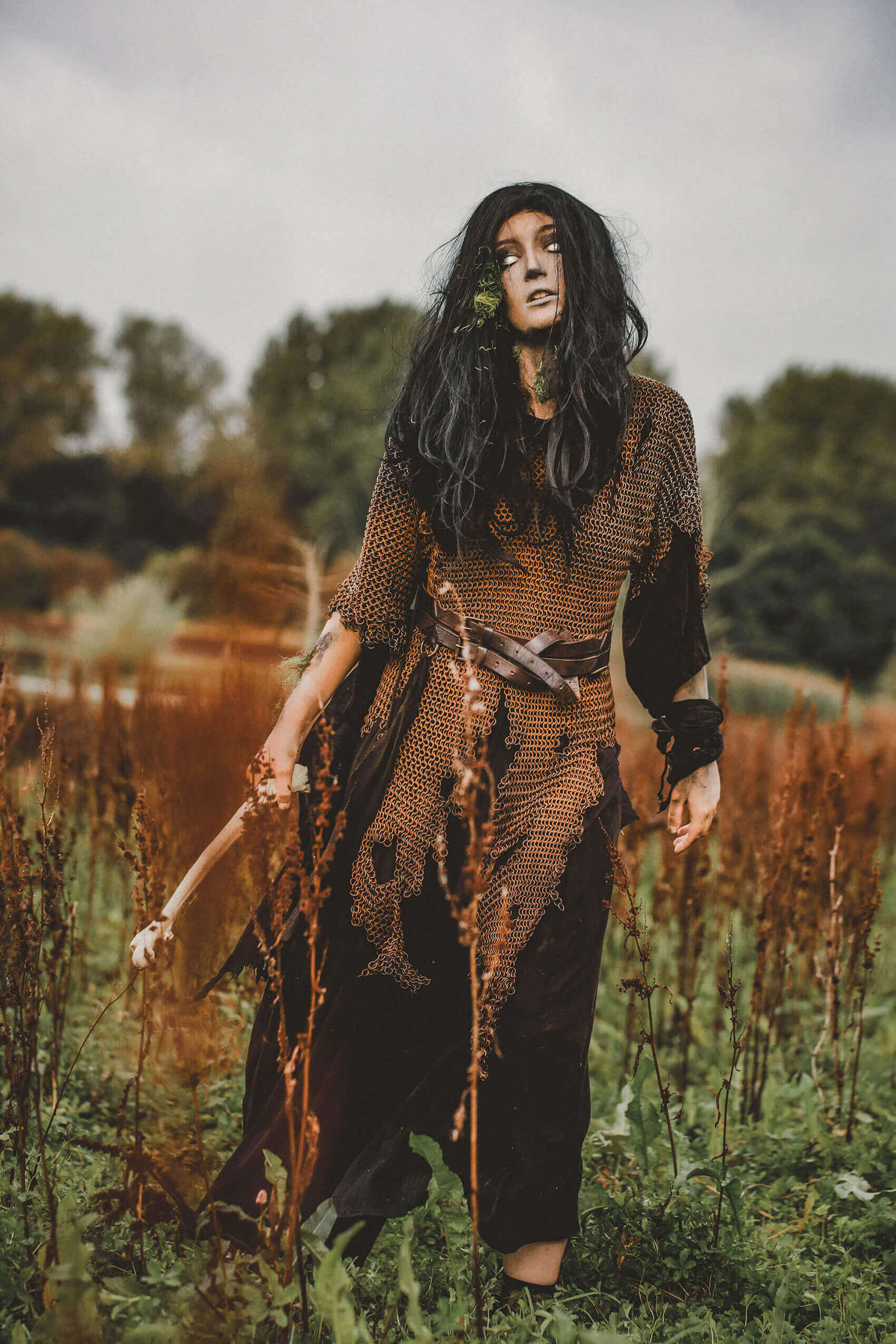 Person in a rustic outfit with long hair standing in a field