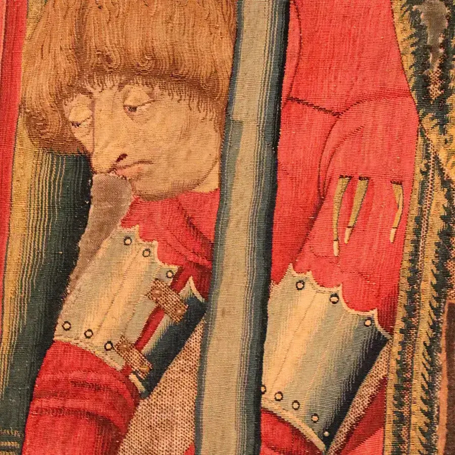 Close-up of a medieval tapestry featuring a man in red armor with a thoughtful expression.