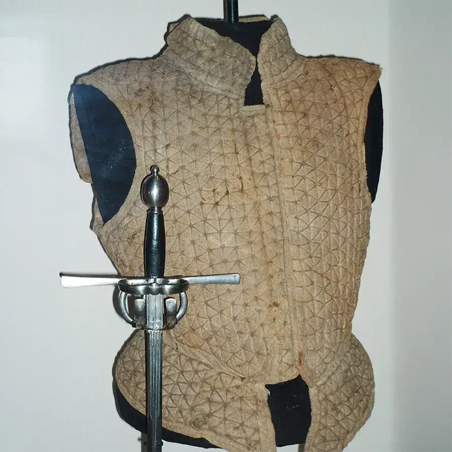 Historical quilted armor displayed with a medieval sword, showcasing craftsmanship and wear over time.