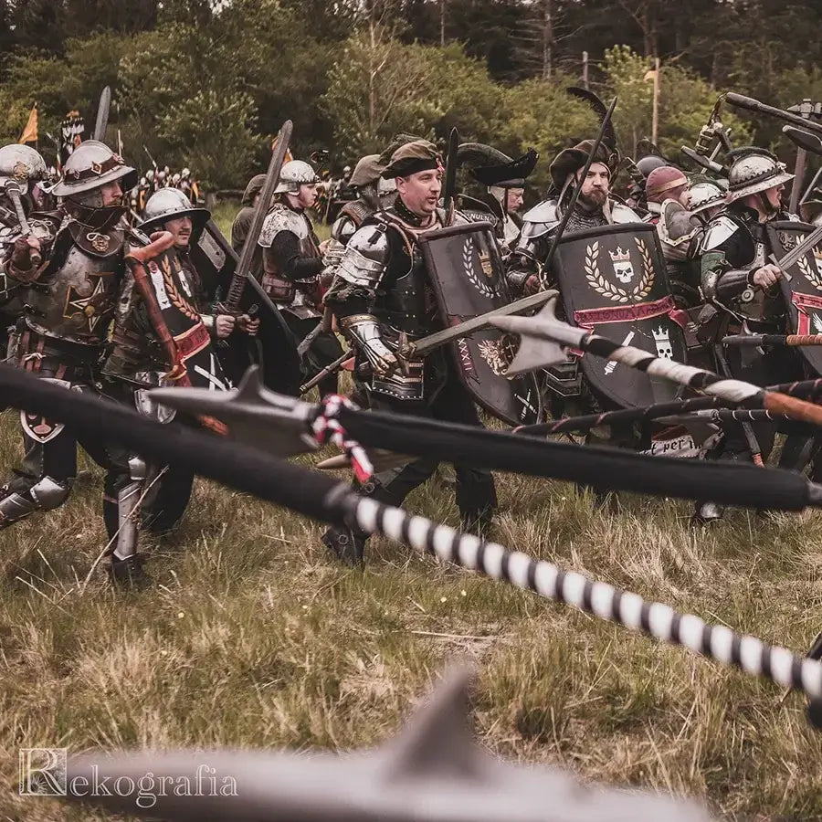 A group of armored warriors in battle formation, wielding shields and weapons in a medieval reenactment.