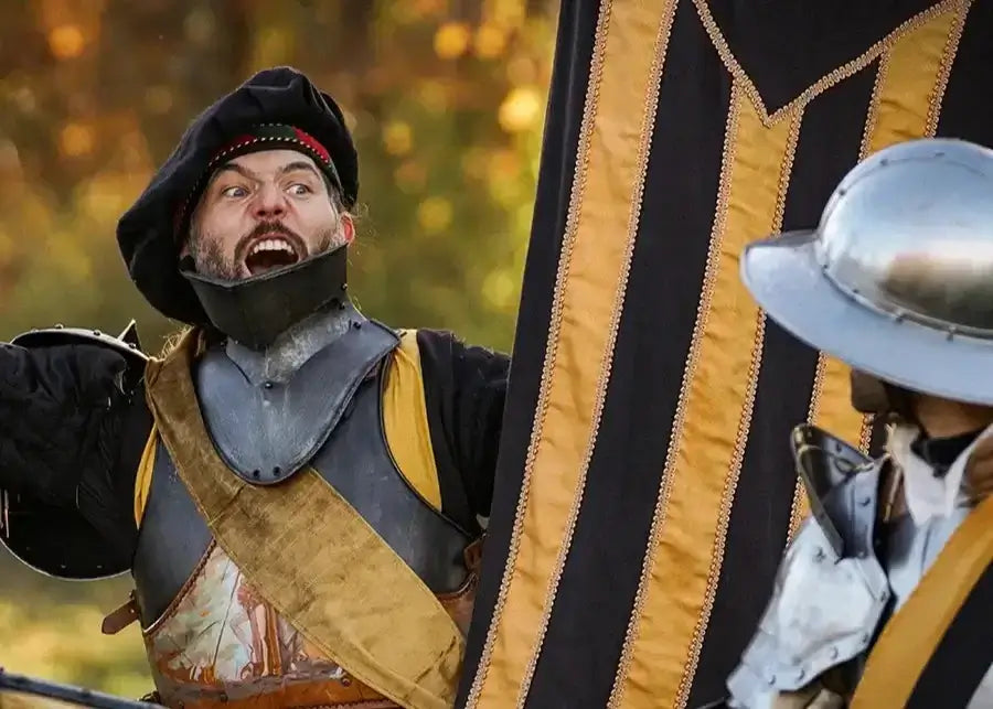Armoured LARP participant shouting while holding a large black and gold banner beside another armoured figure.
