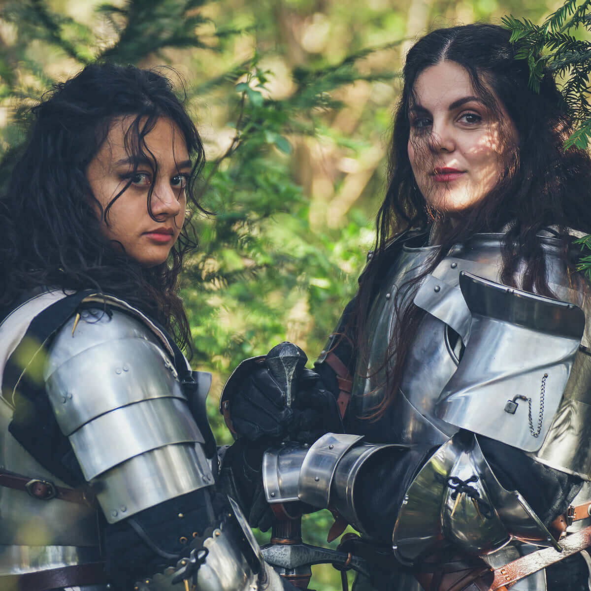 Two women in medieval armor holding swords in a forest setting, exuding strength and camaraderie.