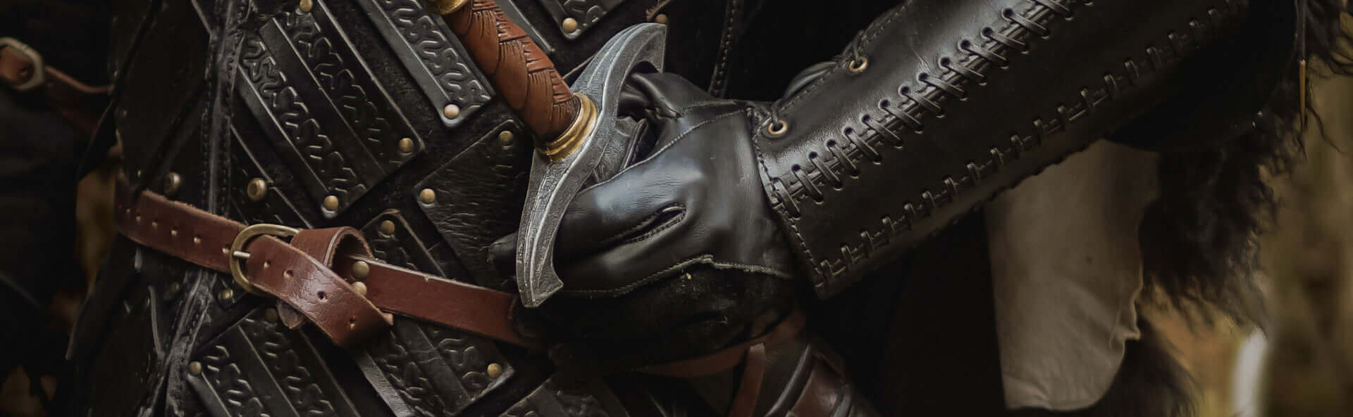 Close-up of armored knight gripping a sword with intricate leather details, showcasing medieval craftsmanship.