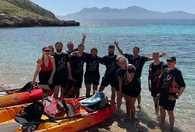 Group of kayakers enjoying their adventure at a scenic beach with clear waters and mountains in the background.